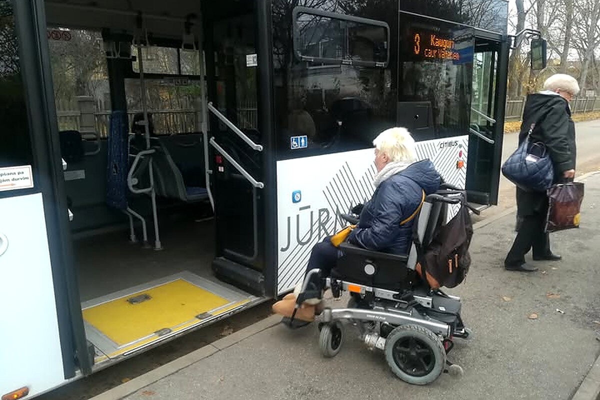 Sieviete ratiņkrēslā pie autobusa ar izvilktu rampu
